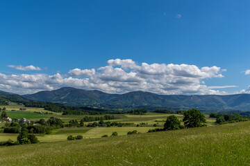 Ondrejnik and views of other Beskydy hills and mountains with white clouds and blue sky in the background during a sunny day.