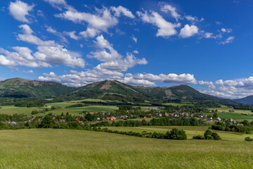 Ondrejnik and views of other Beskydy hills and mountains with white clouds and blue sky in the background during a sunny day.