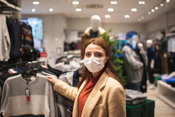 Fototapeta na wymiar Beautiful girl wearing protective medical mask and fashionable clothes looks at behind of showcase. New normal lifestyle concept.