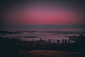 Deep red sky at sunrise with a landscape in which lies a heavy fog over the city.