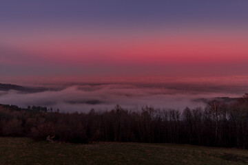 Naklejka na ściany i meble Deep red sky at sunrise with a landscape in which lies a heavy fog over the city.
