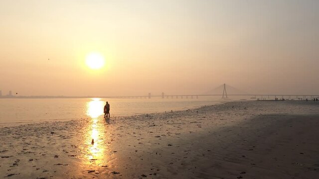 4K Real Time Wide Angle footage of a family of a father and children playing in front of Mumbai's Bandra Worli Sea Link Bridge (BWSL) on a smoggy hazy evening during sunset. Mumbai, Maharashtra, India