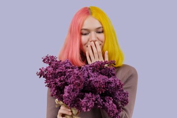 Surprised teenager girl with dyed pink yellow hair holding lilac flowers in hands