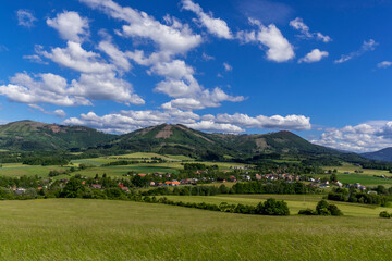 Fototapeta na wymiar Ondrejnik and views of other Beskydy hills and mountains with white clouds and blue sky in the background during a sunny day.