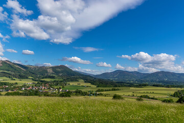 Under the sun and shadows Ondřejník and a view of other Beskydy hills and mountains with white clouds and blue sky in the background.