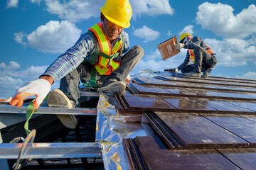 Two male workers wearing safety clothes Installing the roof tile house That is a ceramic tile roof...