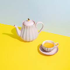 Teapot with cup of tea on multi colored pastel blue and yellow background. Minimal herbal organic beverage concept. Trend shadows.