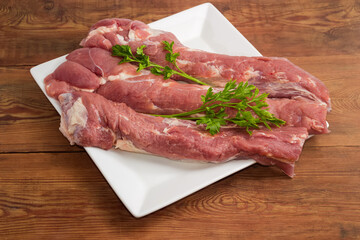 Pieces of uncooked pork tenderloin on dish on rustic table