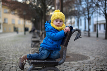Cute child, toddler boy, sitting on a bench in the center of Prague