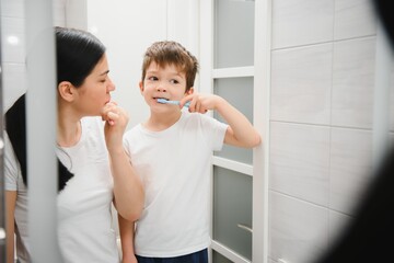 Beautiful mother and happy son brushing teeth near mirror in bathroom