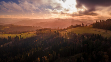 Aerial view of hilltops during sunrise rays shine through the landscape through clouds on the ground during the autumn morning Beskydy region.