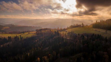 Aerial view of hilltops during sunrise rays shine through the landscape through clouds on the ground during the autumn morning Beskydy region.