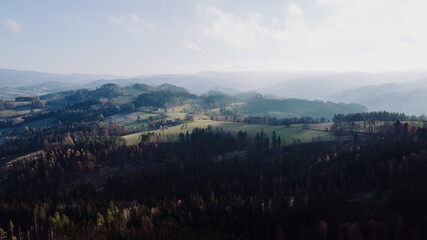 Aerial view of hilltops during sunrise rays shine through the landscape through clouds on the ground during the autumn morning Beskydy region.