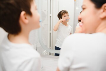 Beautiful mother and happy son brushing teeth near mirror in bathroom