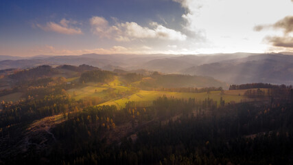 Aerial view of hilltops during sunrise rays shine through the landscape through clouds on the ground during the autumn morning Beskydy region.