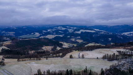 Aerial view of a hilly landscape with freshly fallen snow during a light snowfall in the Beskydy region.