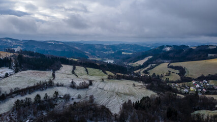 Aerial view of a hilly landscape with freshly fallen snow during a light snowfall in the Beskydy region.
