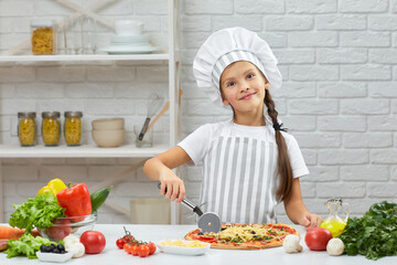 cute little girl in chef hat and an apron cutting pizza at kitchen