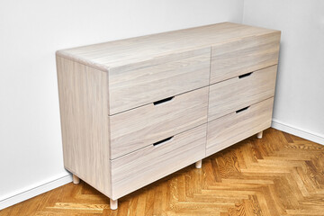 Elegant chest of drawers made with bleached solid oak timber with finger pull drawers stands on wood block parquet floor in light room