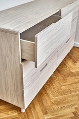 Contemporary chest of drawers made with bleached solid oak timber with open finger pull drawer stands on parquet floor in room closeup