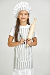 cute little girl in chef hat and apron holding rolling pin on studio background. child dreams of becoming a chef