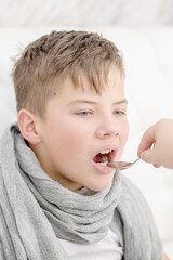 Sick  boy take medication pouring in a spoon from mom while lying on the bed at home