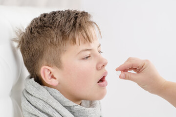 A sick little boy takes a pill from his mother's hands. Treating an unhealthy child Cold season.