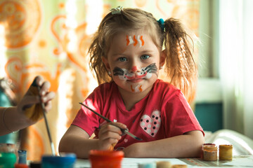 Little cute girl artist with paint of the face in her home.