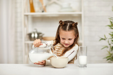 cute little girl eating breakfast: cereal with the milk. child pours milk into a bowl of cereal in the kitchen. healthy breakfast