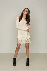 beautiful girl teenager with long legs in a stylish knitted white dress and black shoes posing in the studio on a white background