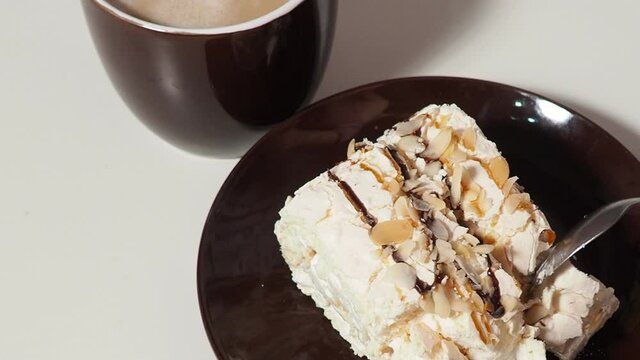 Slice piece of vanilla cake topping with white chocolate chips for coffee or tea break, on white with almond petals, coconut flakes, takes it out of the box, puts it on a saucer, eats, pours coffee