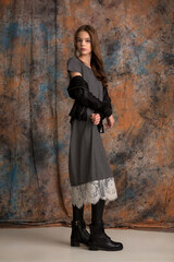 beautiful girl teenager in a stylish gray dress and black boots posing in the studio on a spotted background