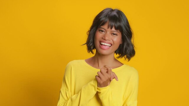 Overemotive dark skinned woman cannot stop laughing clasps hands and giggles positively hears positive story joke or funny anecdote dressed casually poses against yellow background. Emotions, jests
