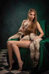 beautiful blonde girl with long hair covered with fur skins posing in a chair with a green cape