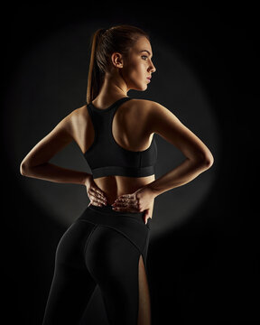 Strong sporty beautiful woman in black sportswear on dark background. sport and fitness concept. back view