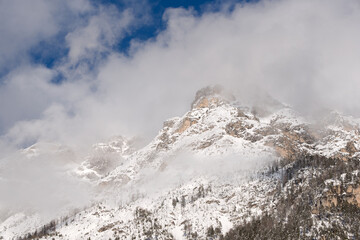 Fototapeta na wymiar le nuvole sulla montagna in inverno, la luce che filtra le nuvole attorno una montagna innevata, lo splendido panorama invernale sulle dolomiti