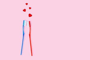 Two toothbrushes of blue and red color and small hearts fly over them, a couple in love metaphor....