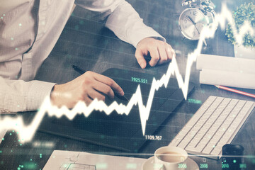 Double exposure of man's hands holding and using a phone and financial graph drawing. Analysis concept.