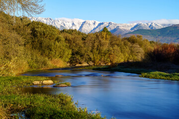 Sunny landscape with rays of sun, river with water and grass in winter sunrise.
