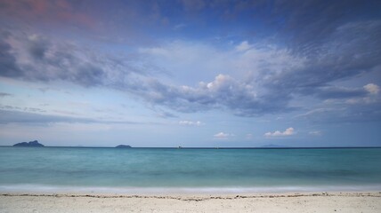 panoramic view of beautiful turquoise sea water on white clear beach with fluffy moving cloud in the background at dusk