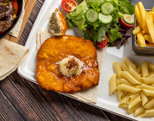 Chicken schnitzel with butter, penne pasta and french fries on wooden table.