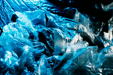 Plastic pollution. Waste management. Environmental protection. Blue creased texture polyethylene film cellophane bag collection on blur dark abstract background.