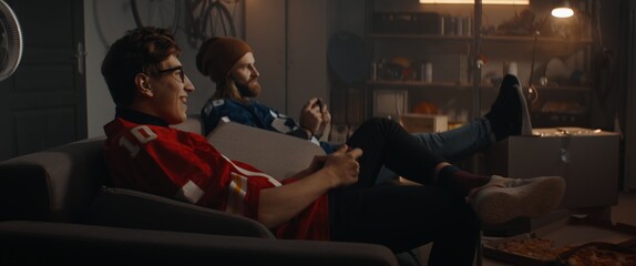  Two friends hanging out, sitting on sofa, playing video game inside garage