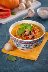 A bowl of pumpkin cream soup with roasted mushrooms and red bell pepper on blue background. Vertical composition.