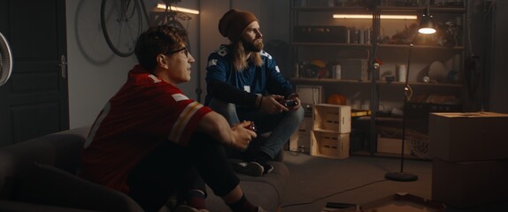  Two friends hanging out, sitting on sofa, playing video game inside garage