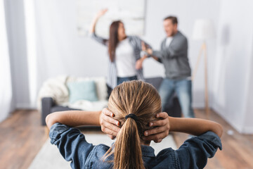  covering ears with hands while parents quarrelling and fighting on blurred background