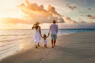 A elegant family in white summer clothing walks hand in hand down a tropical paradise beach during...