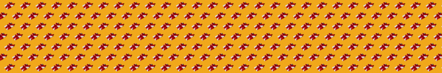 Yellow holiday background. Gift seamless pattern. Festive composition. Care package. Symmetrical diagonal arrangement of presents in white boxes with red ribbon bows isolated on bright orange.