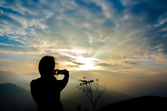 Young woman taking a picture with mobile phone of sunrise in the mountains