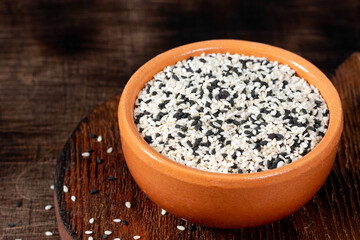 White and black sesame seeds in a ceramic bowl on a brown wooden table